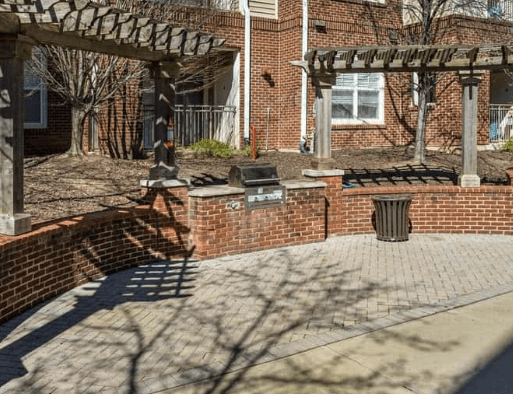 Brick patio with pergola, grill, and trash receptacle.