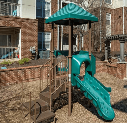 Green and brown playground slide with steps in a mulch-covered play area.