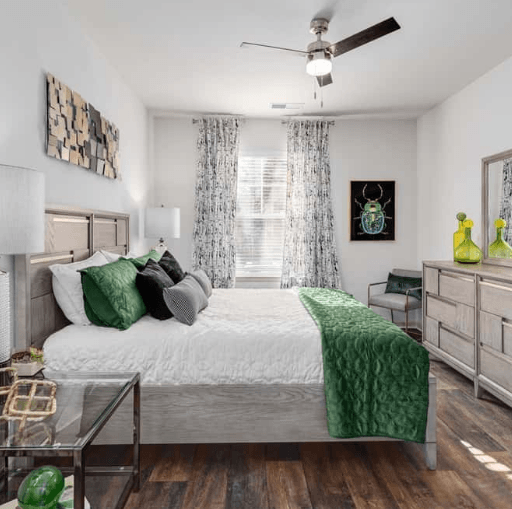 Modern bedroom with white bedding, green accents, and wood flooring.