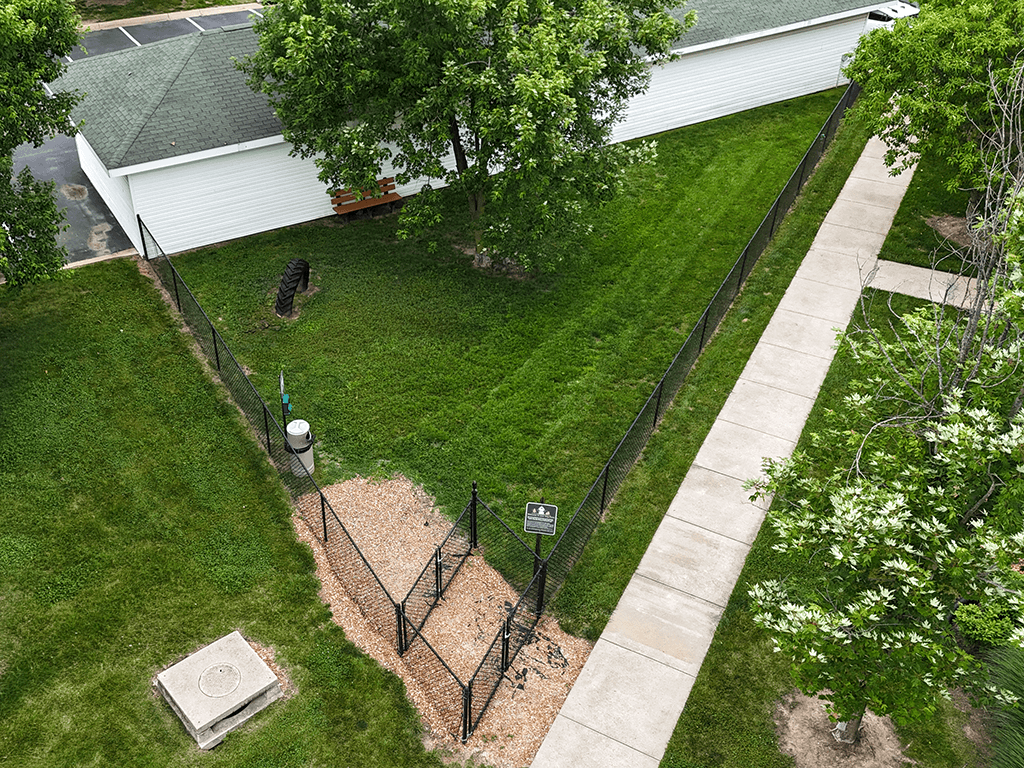 A black fence runs along a sidewalk in a grassy area.