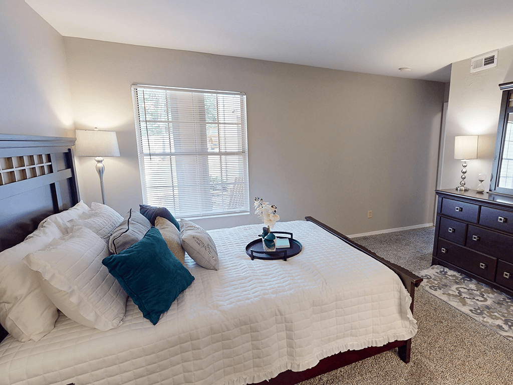 A bedroom with a large bed, a nightstand, and a window with blinds.