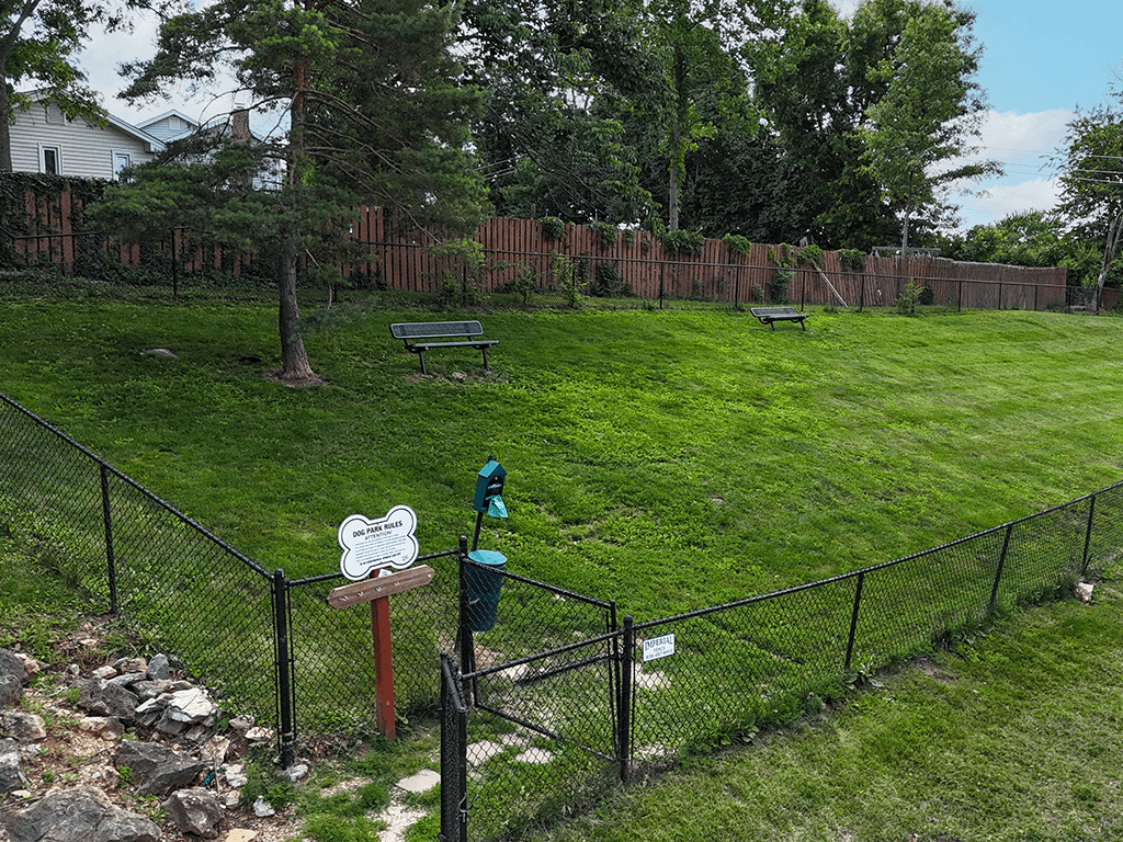 A dog pakr with a fence, a bench, and a sign.