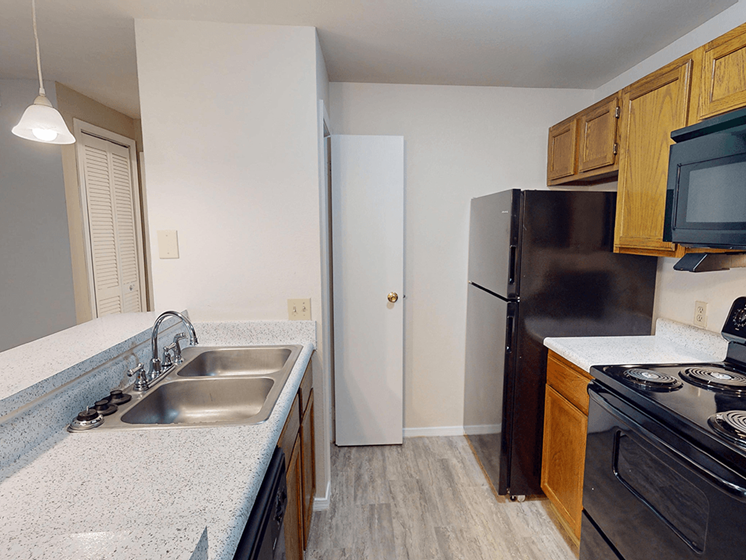 A kitchen with a black refrigerator, white sink, and wooden cabinets.