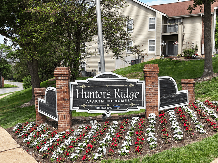 A sign for Hunter's Ridge Apartment Homes is surrounded by flowers.