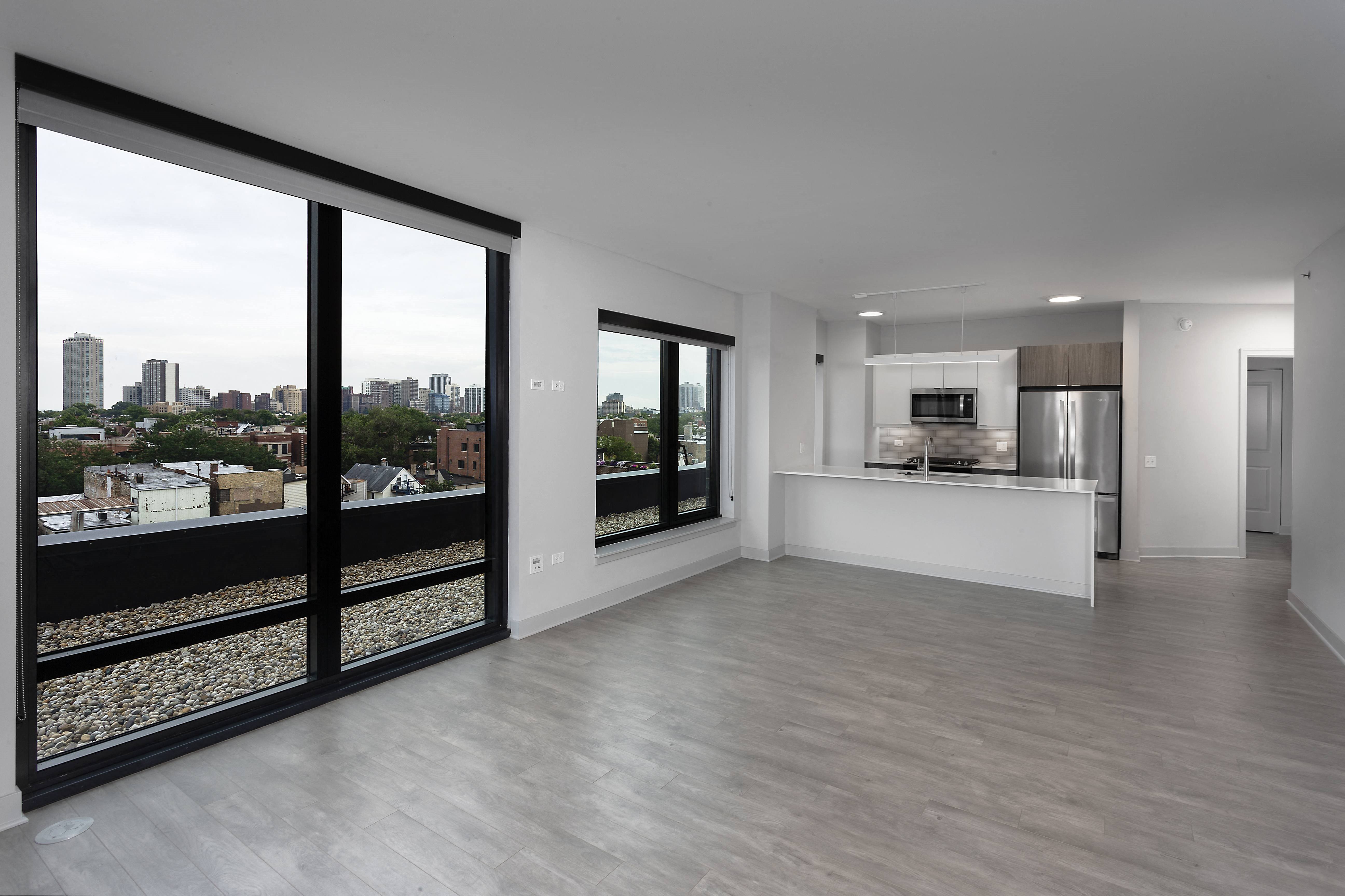 a living room and kitchen with large windows and a city view at Residences at Addison Clark Apartments, Chicago, 60613
