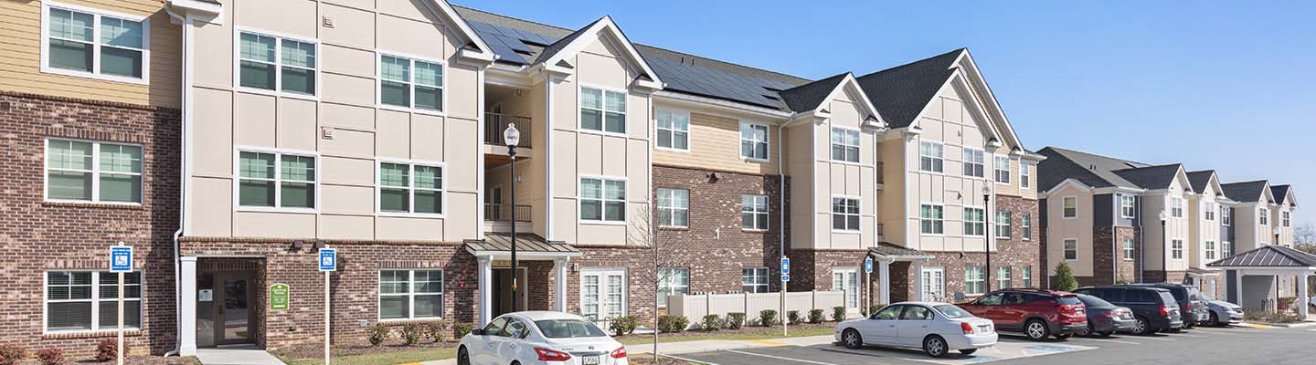 A row of apartment buildings with cars parked in front.