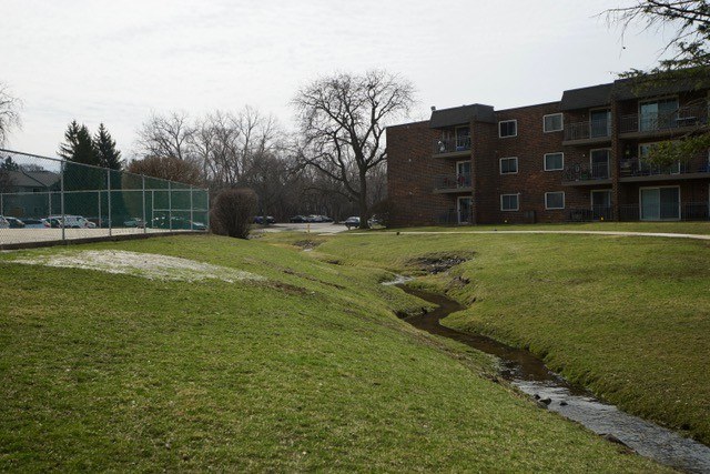 A grassy area in front of a brick building with a small stream running through it.