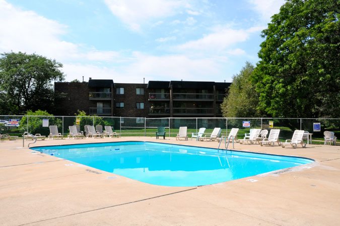 A swimming pool surrounded by chairs and trees with a building in the background.