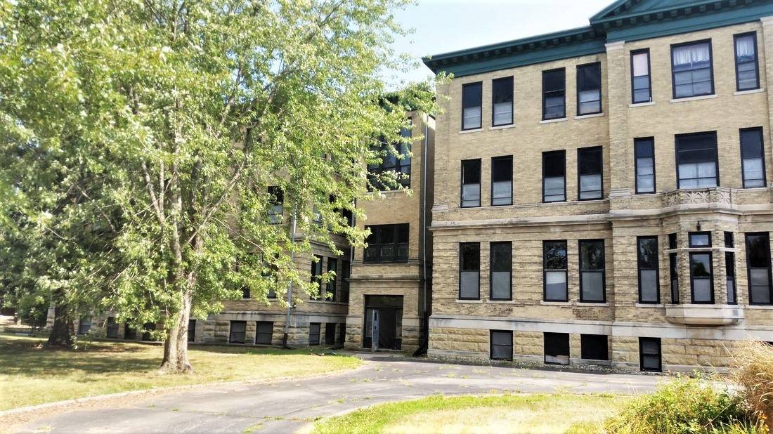 A large, old building with many windows is surrounded by trees.