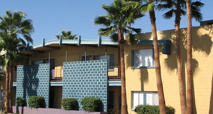 a yellow building with a green lattice facade and palm trees in front of it