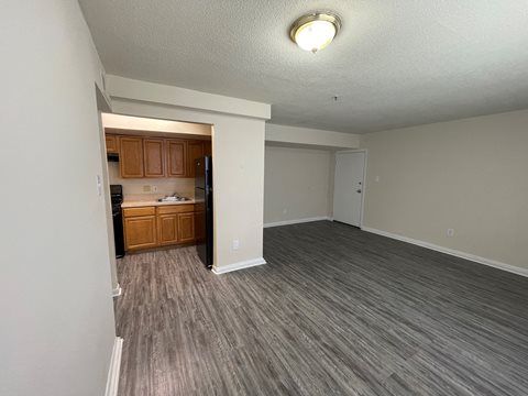 an empty living room with a kitchen in the background