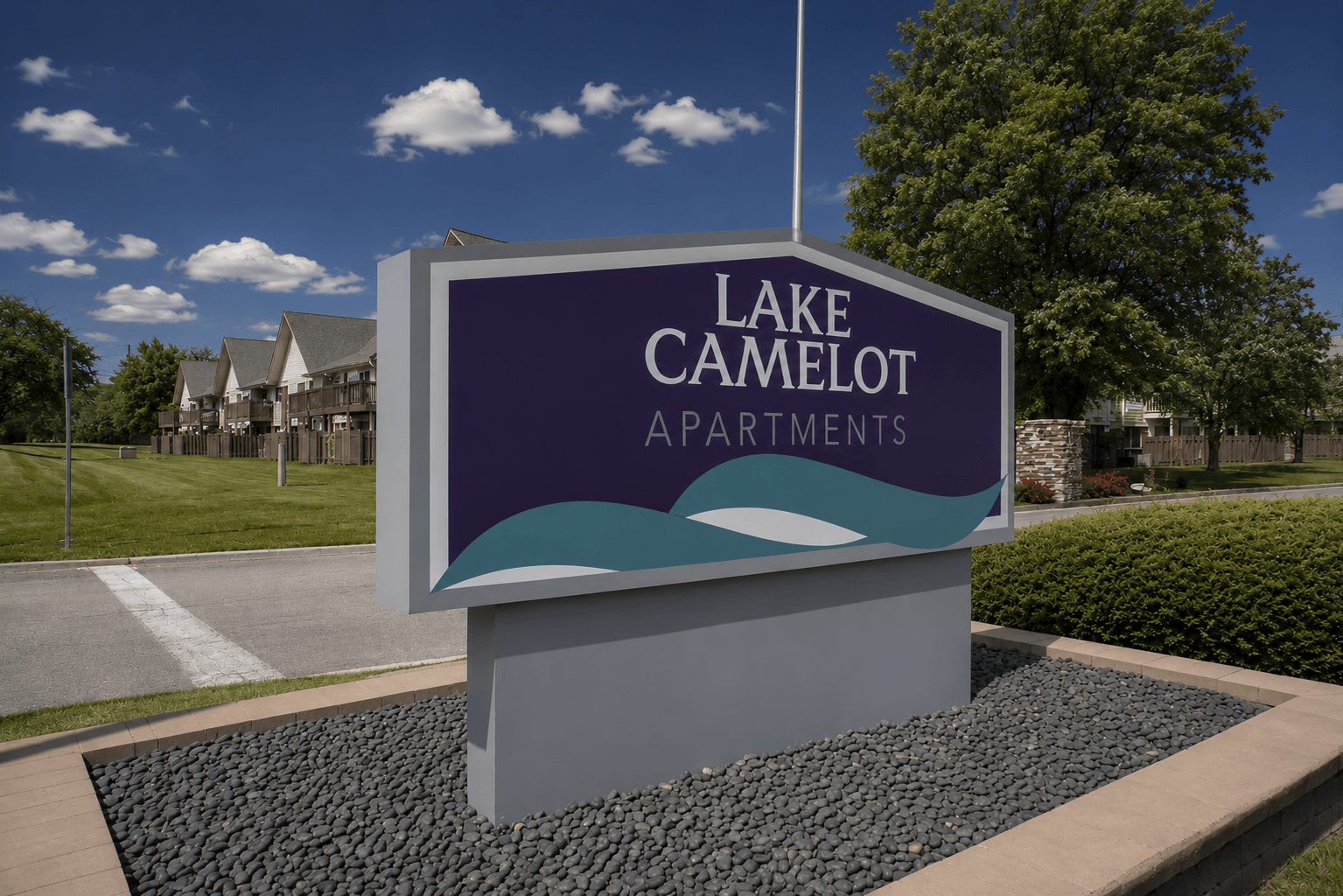 A sign for Lake Camelot Apartments in front of a building.