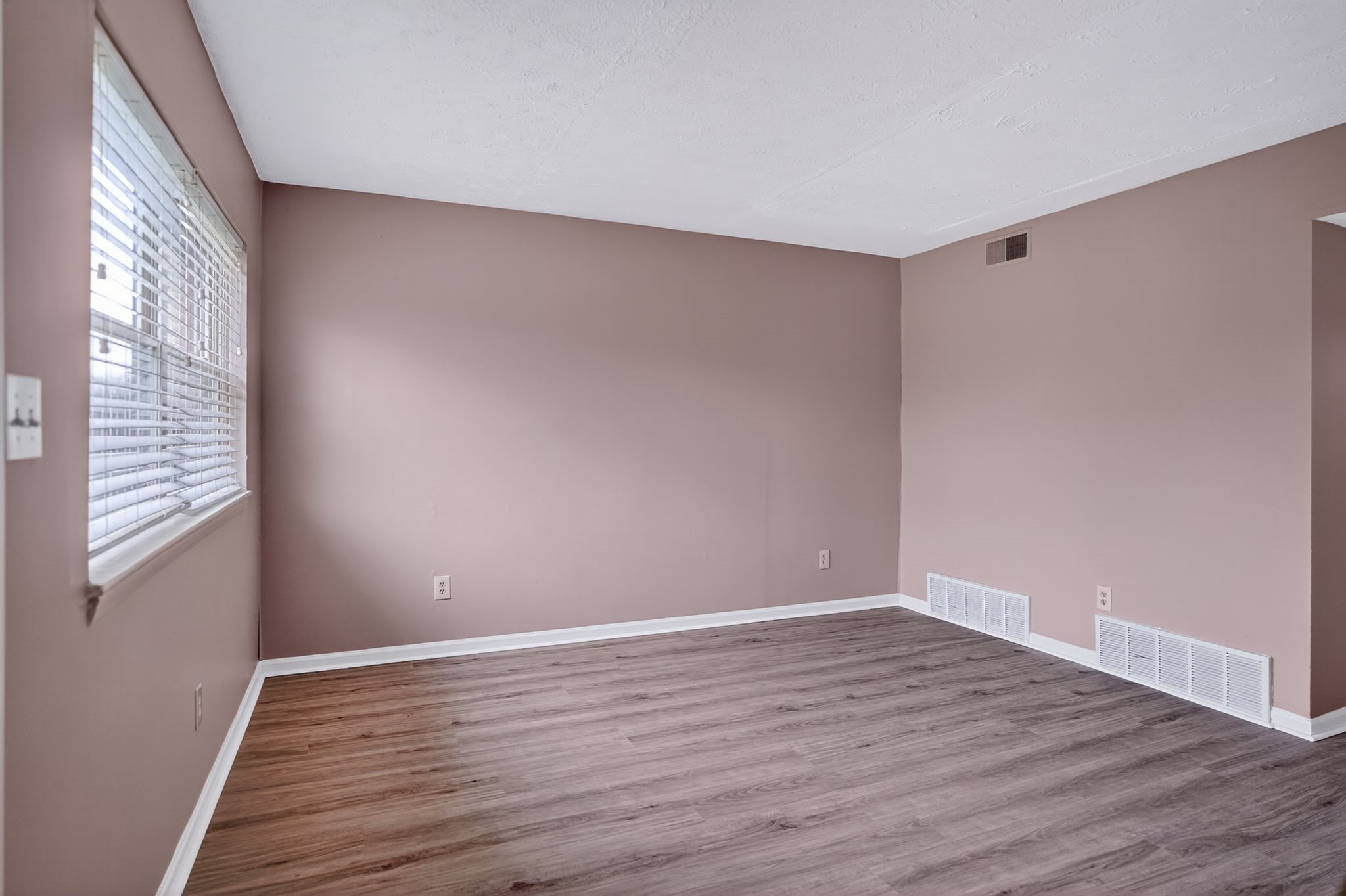 Empty room with wooden flooring and white baseboards.