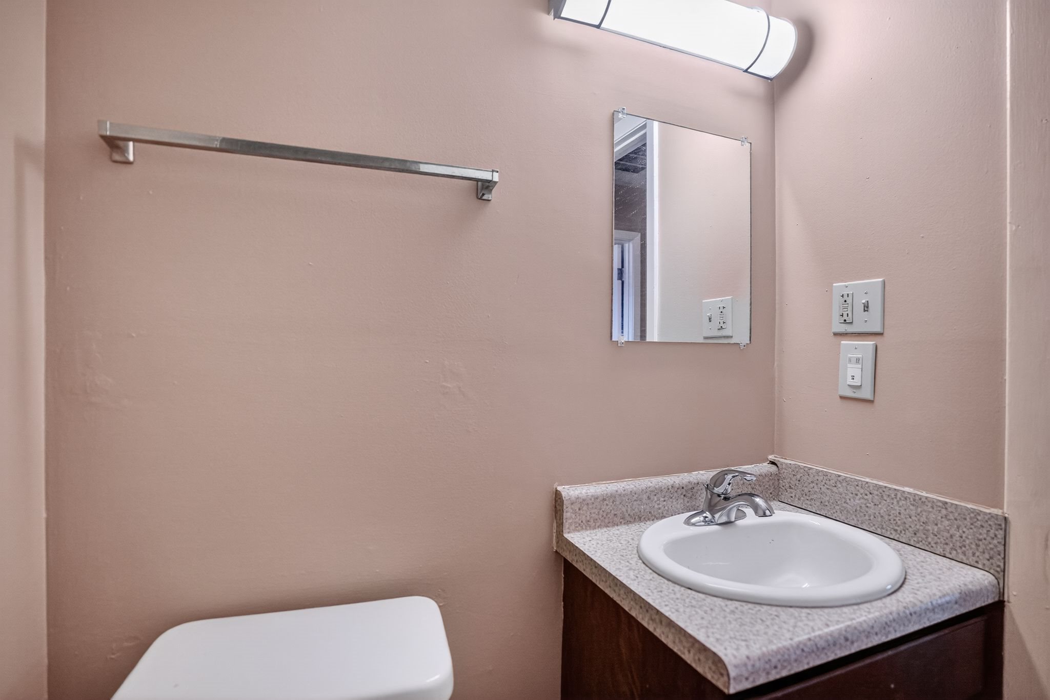 A bathroom with a toilet, sink, mirror and light.