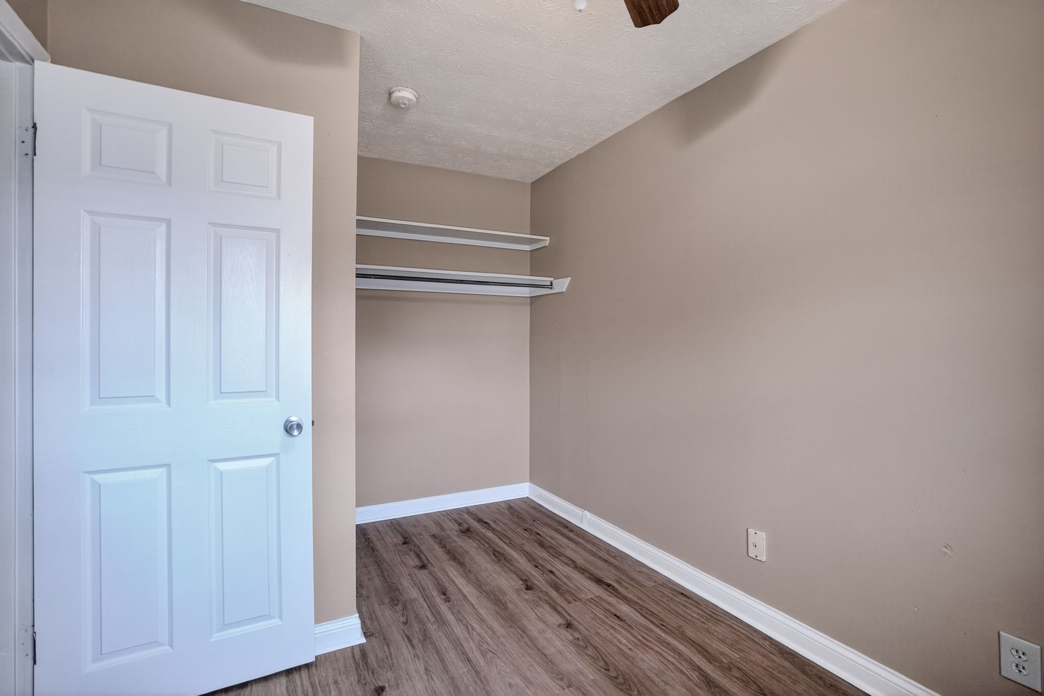 A white door is open to a room with a wooden floor and a ceiling fan.