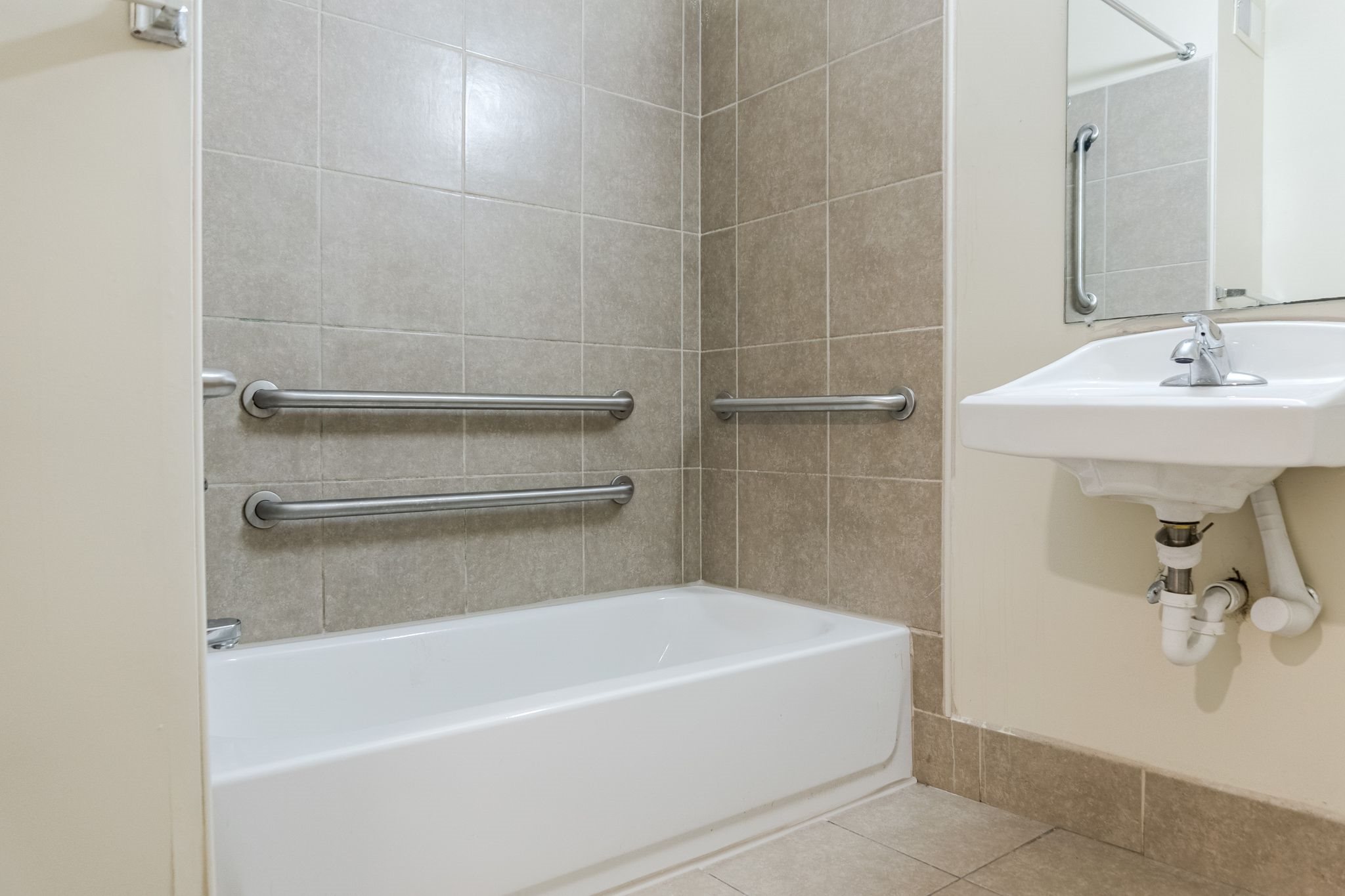 A white bathtub sits next to a sink in a tiled bathroom.