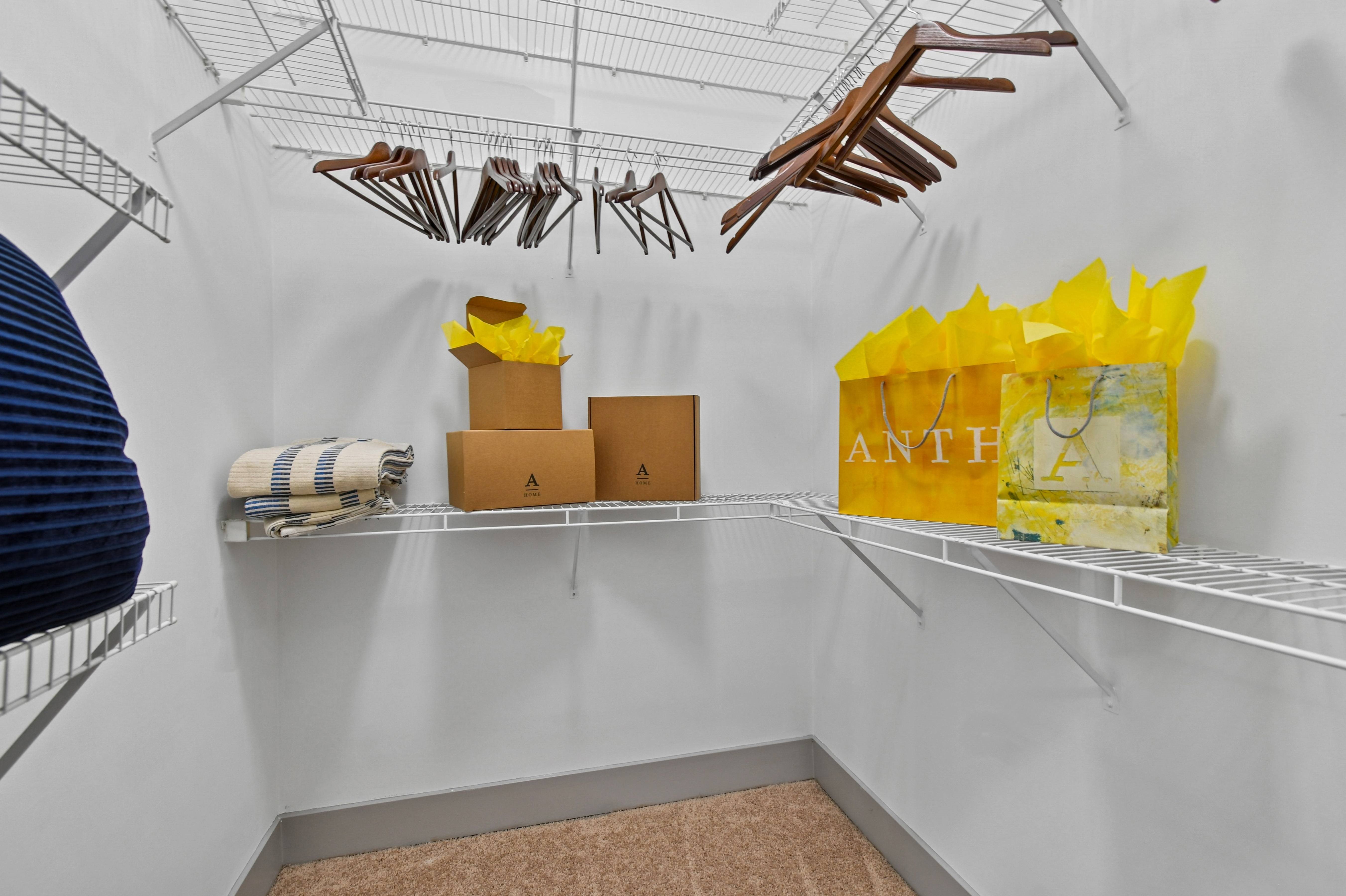 A white closet with clothes hanging and boxes on the shelf.