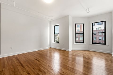 an empty living room with wood flooring and three windows