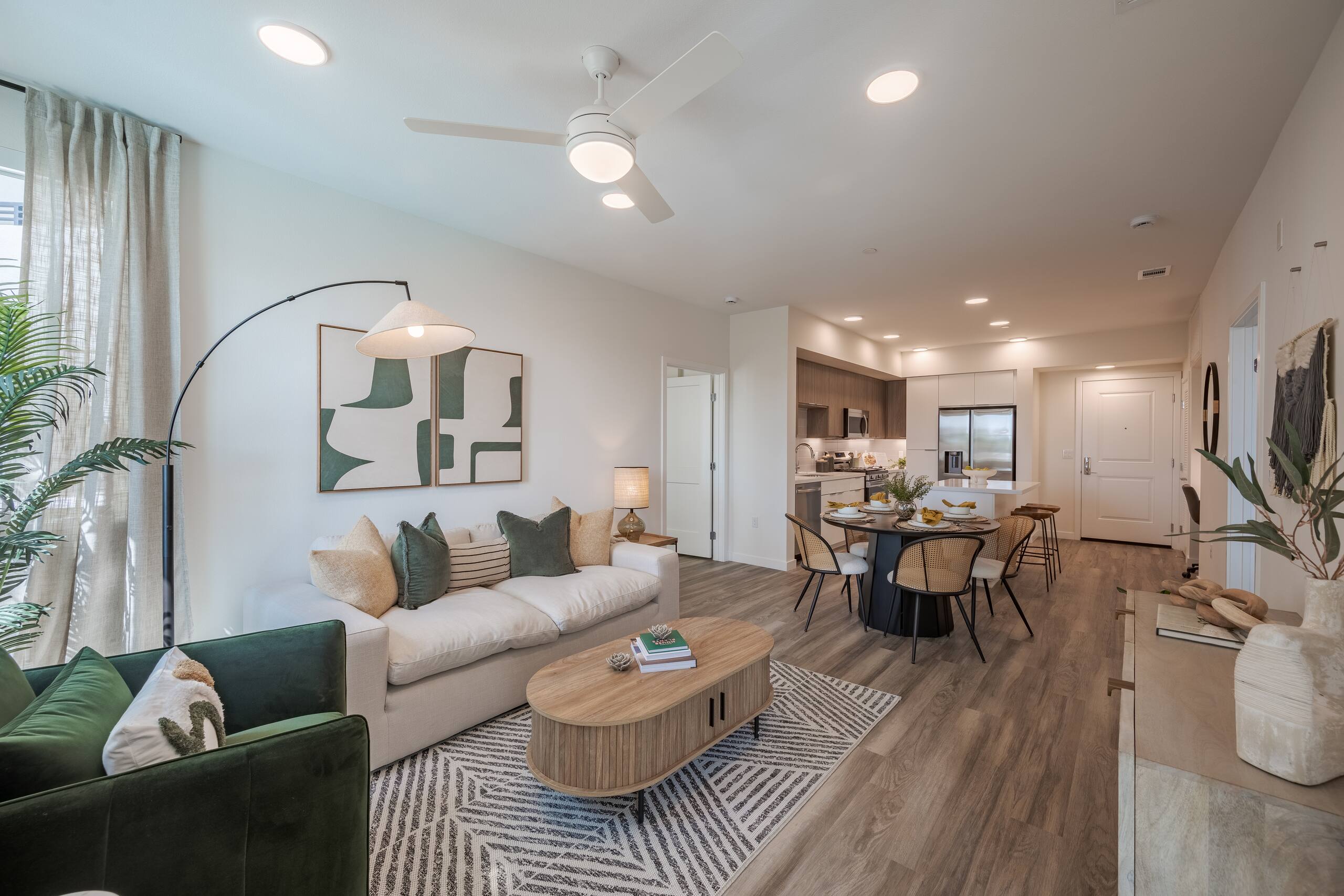 Furnished living and dining area with wood-style flooring, large windows, and an open kitchen.