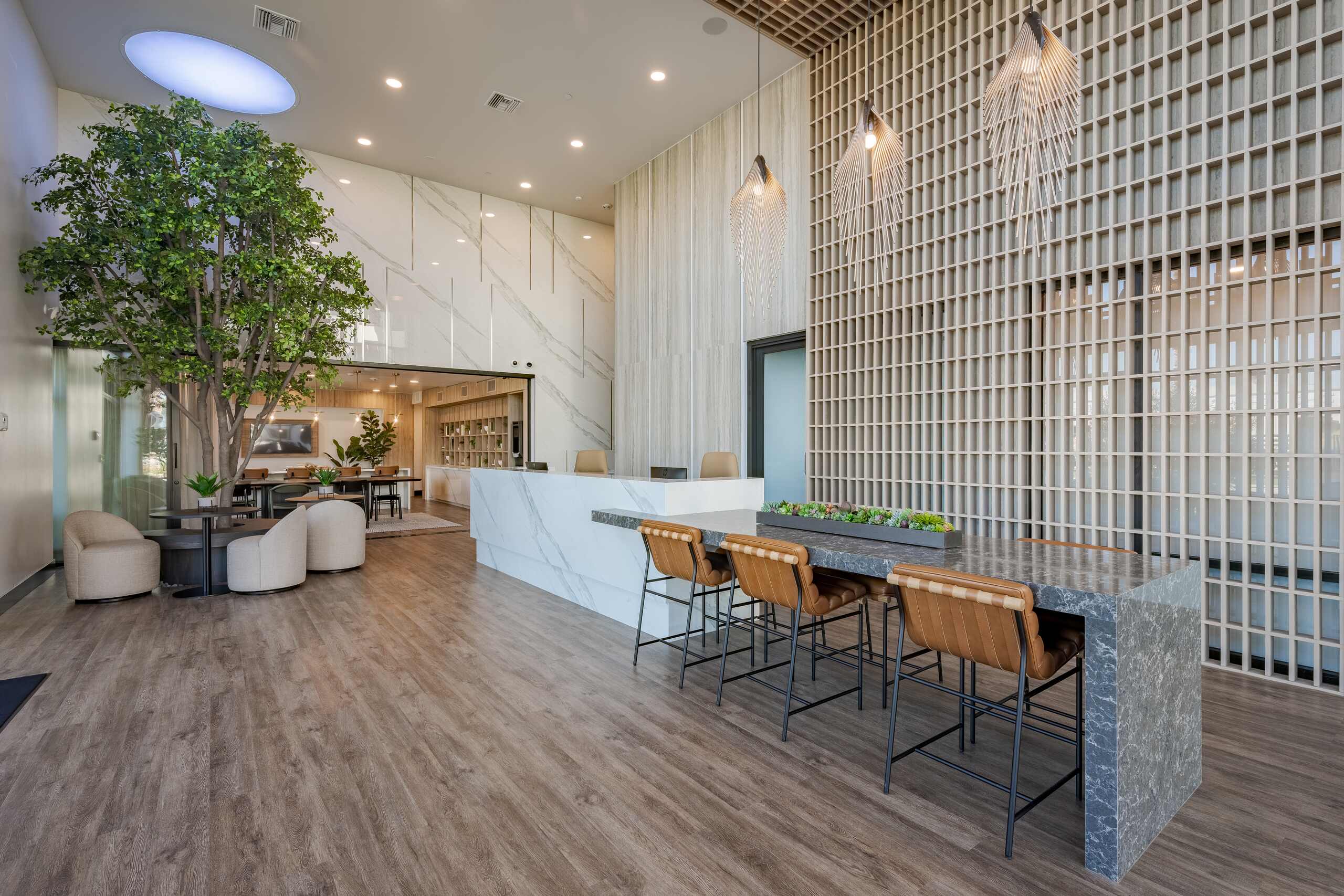 Zia lobby with curved sofas, round tables, a long worktable, greenery, and high ceilings.
