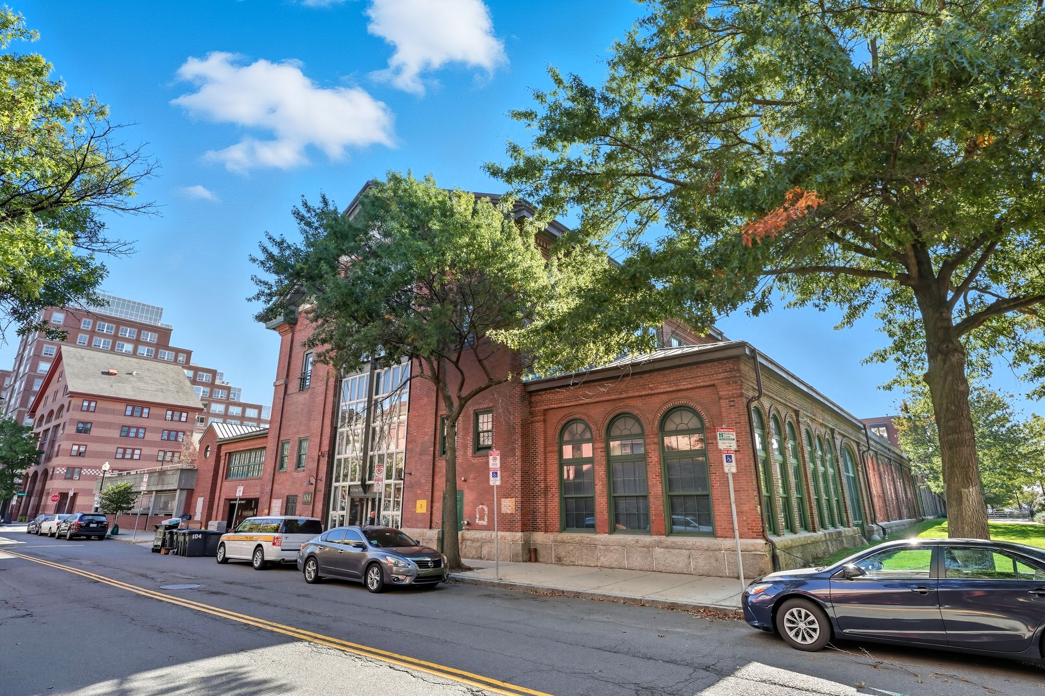 A street view with cars parked on the side of the road and a building with a red brick facade.