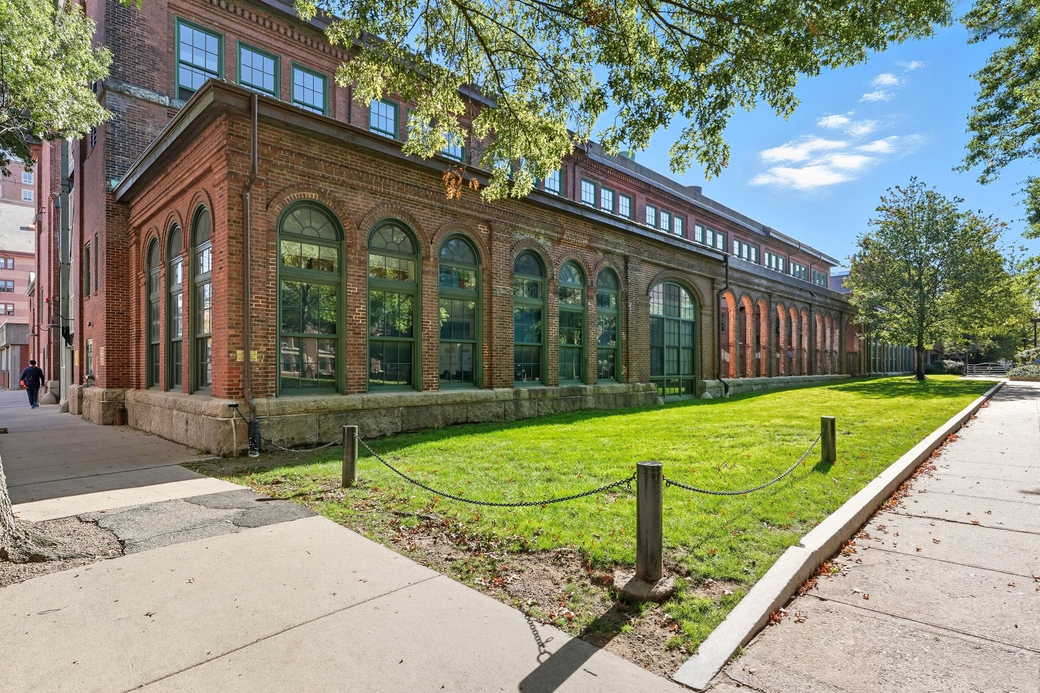 A long brick building with many windows is surrounded by a green fence.