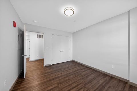 A room with white walls and wood flooring, with a door on the left and two doors in the back.