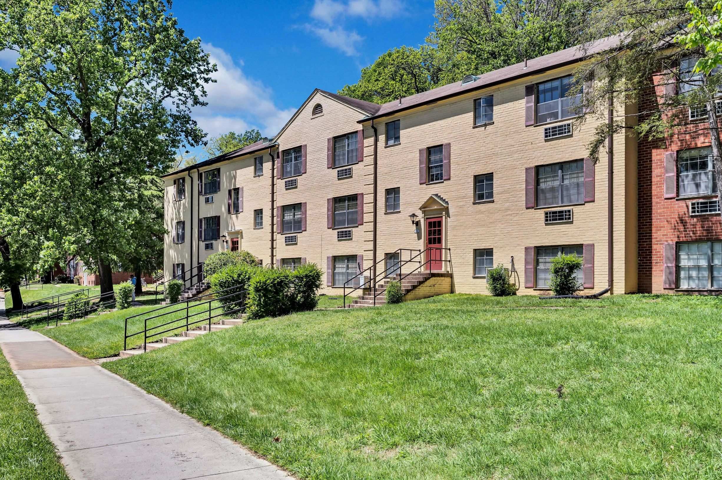 A brick apartment building with a red door and a green lawn in front.