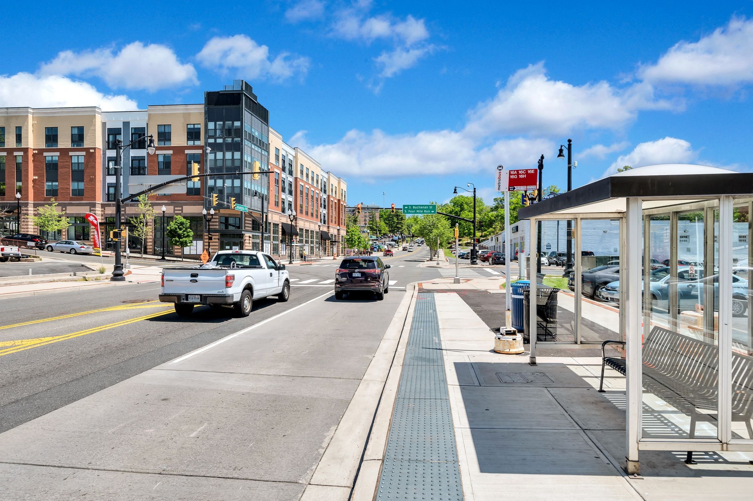 A city street with a bus stop and cars driving down the road.