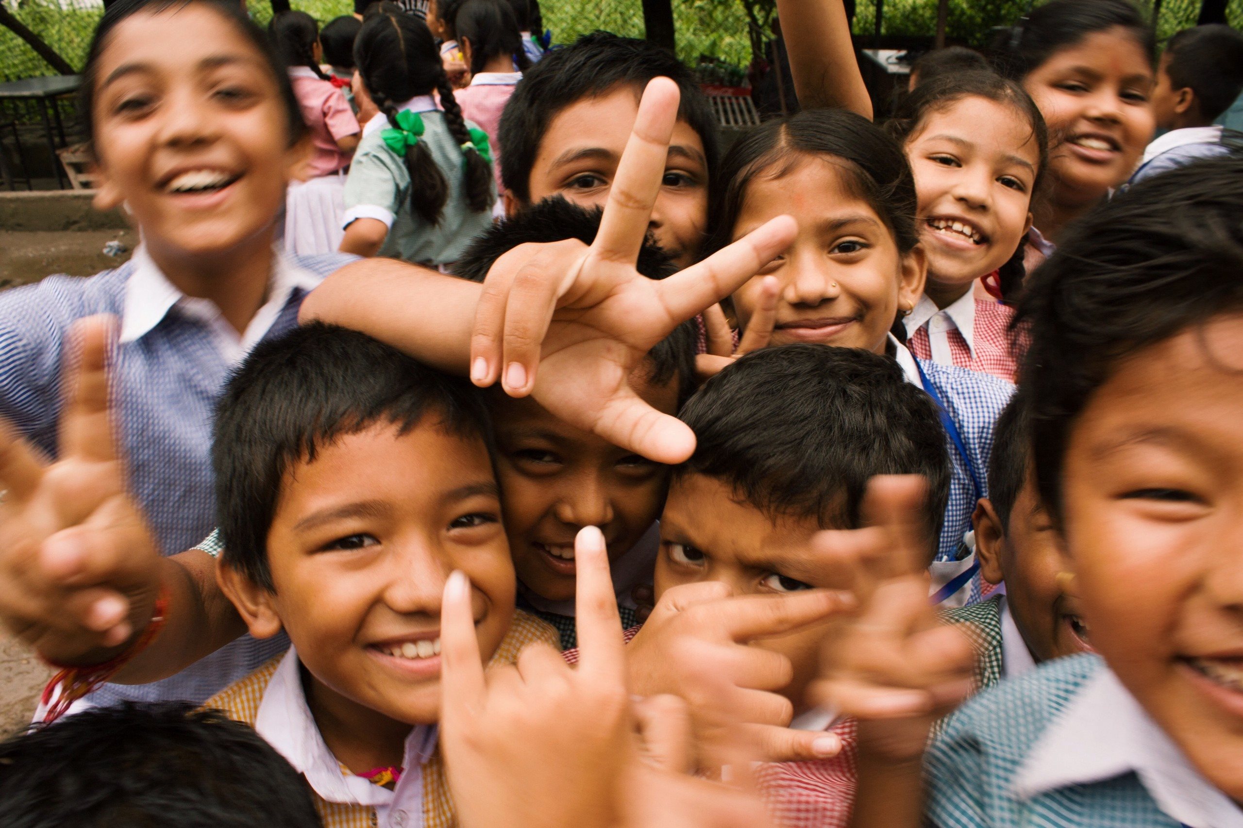 A group of children are making peace signs with their hands.