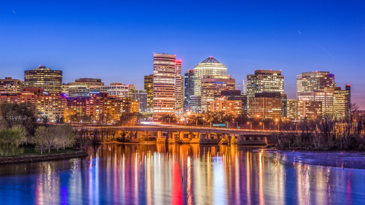 A city skyline at dusk with buildings reflecting in a river.