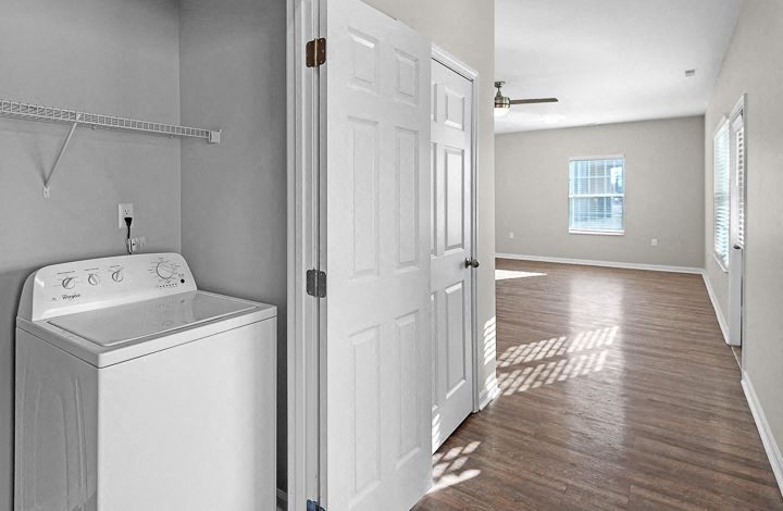 A white washing machine sits in a laundry room with a door open to a hallway.