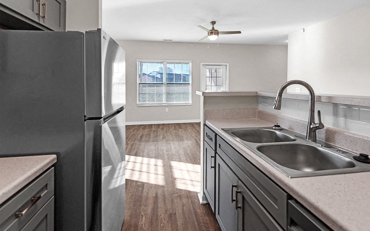 A kitchen with a refrigerator, sinks, and a ceiling fan.