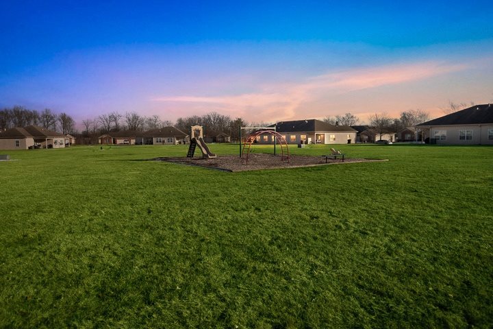 A playground with a swing set and a slide in the middle of a grassy field.