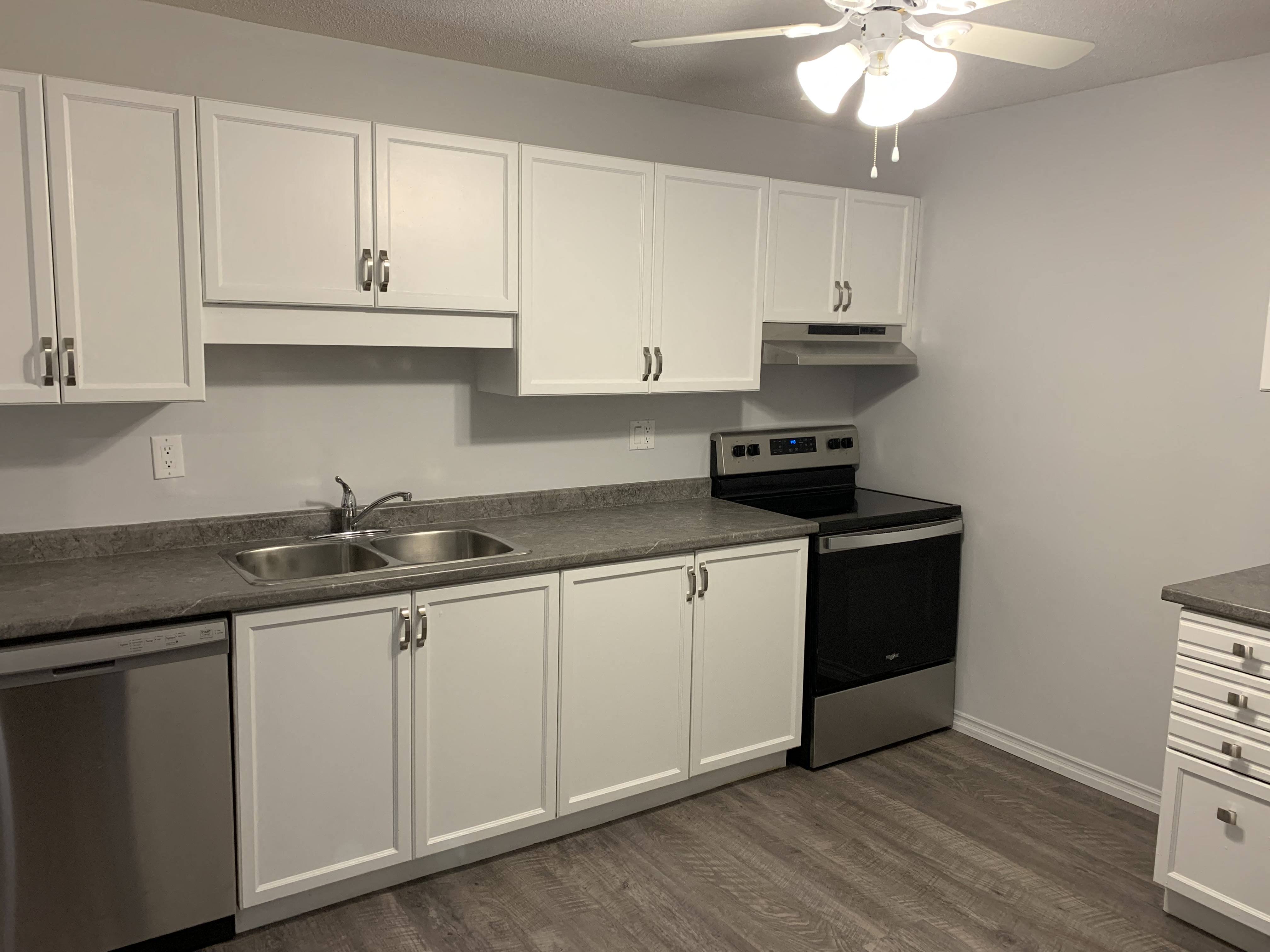 a kitchen with white cabinets and black appliances and a ceiling fan