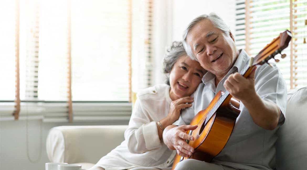 Older couple enjoying their home, playing guitar.