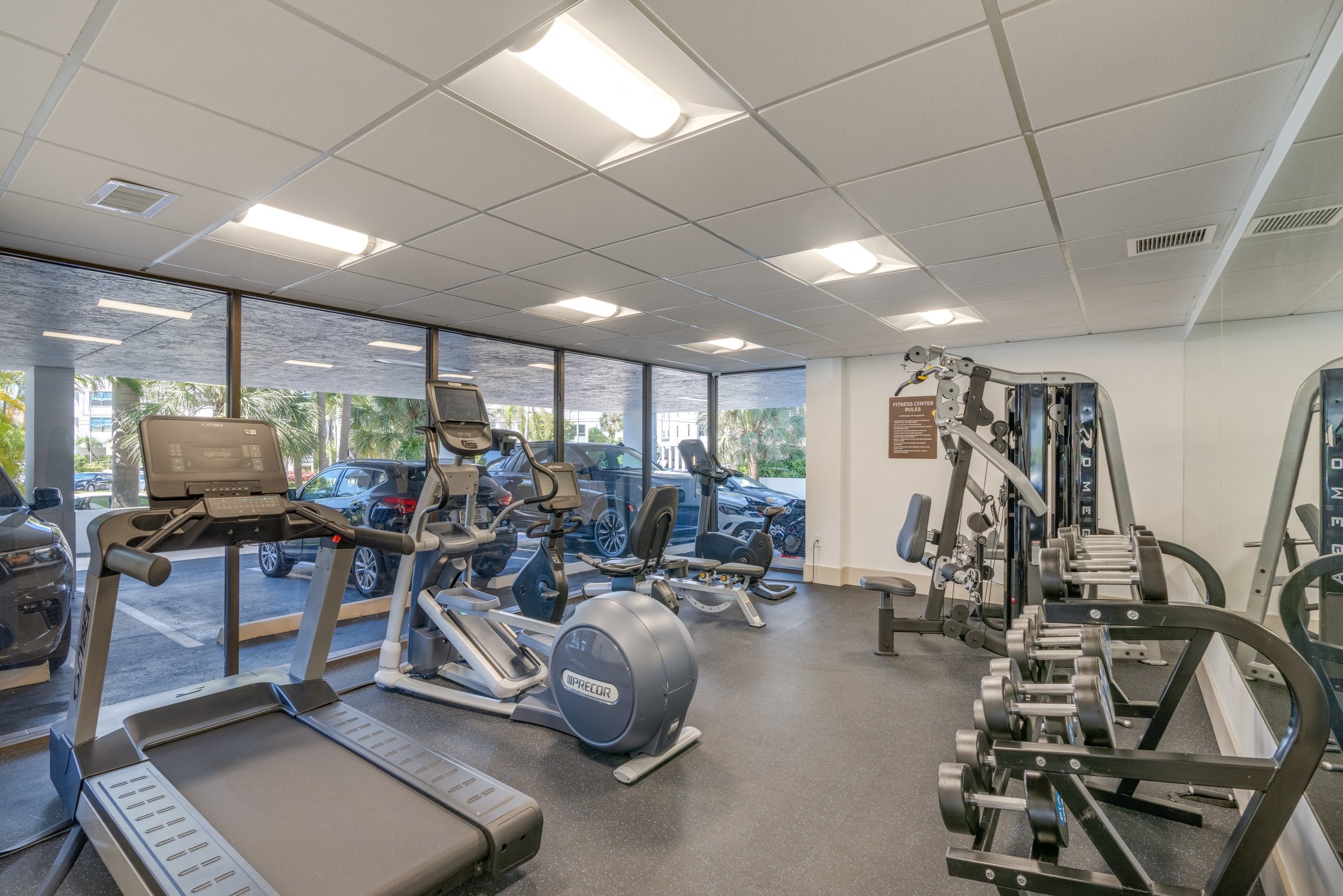a gym with cardio equipment and weights in a building with windows