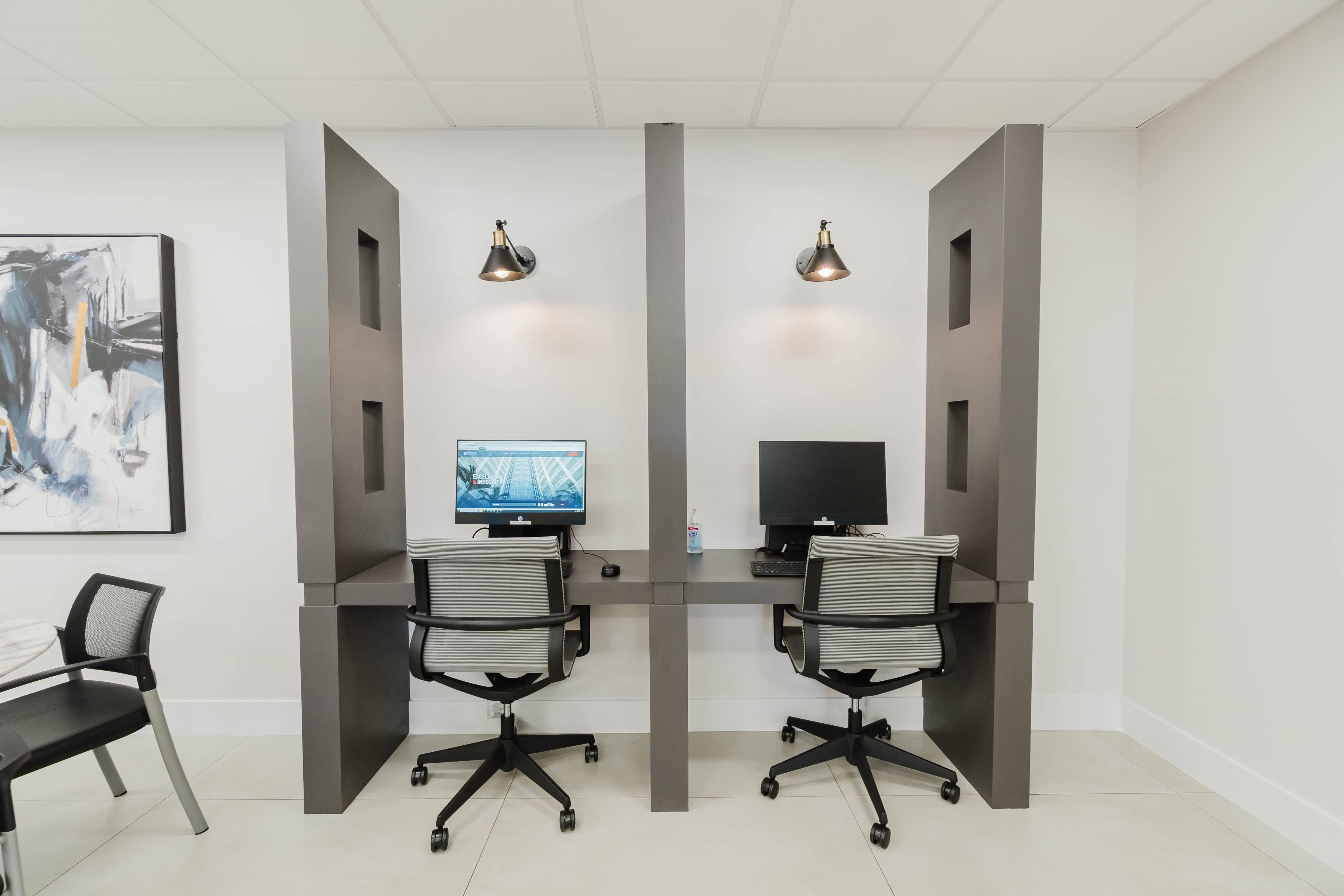 Two computers on a desk with a black chair.