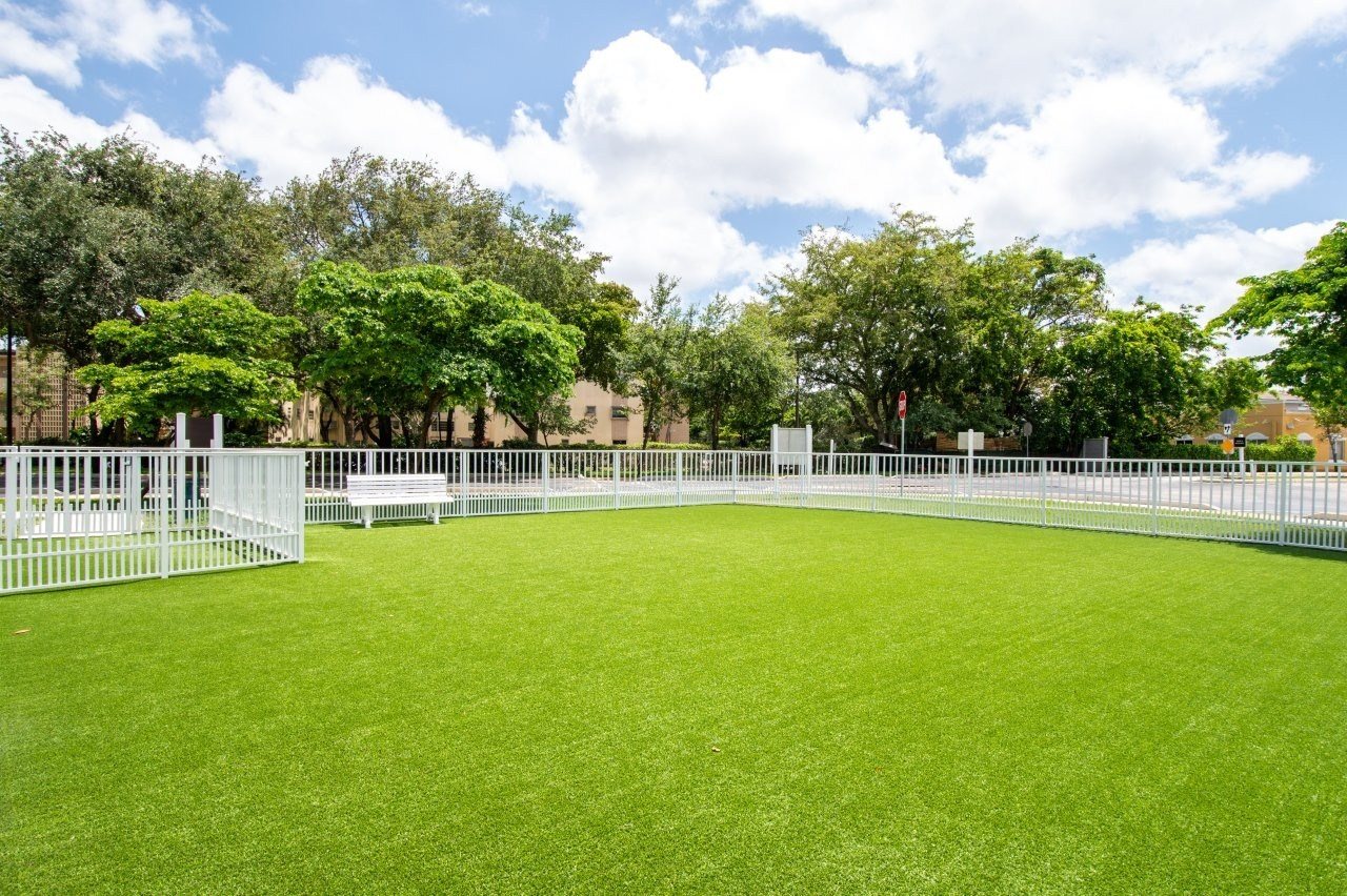 A green field with white fences and trees in the background.
