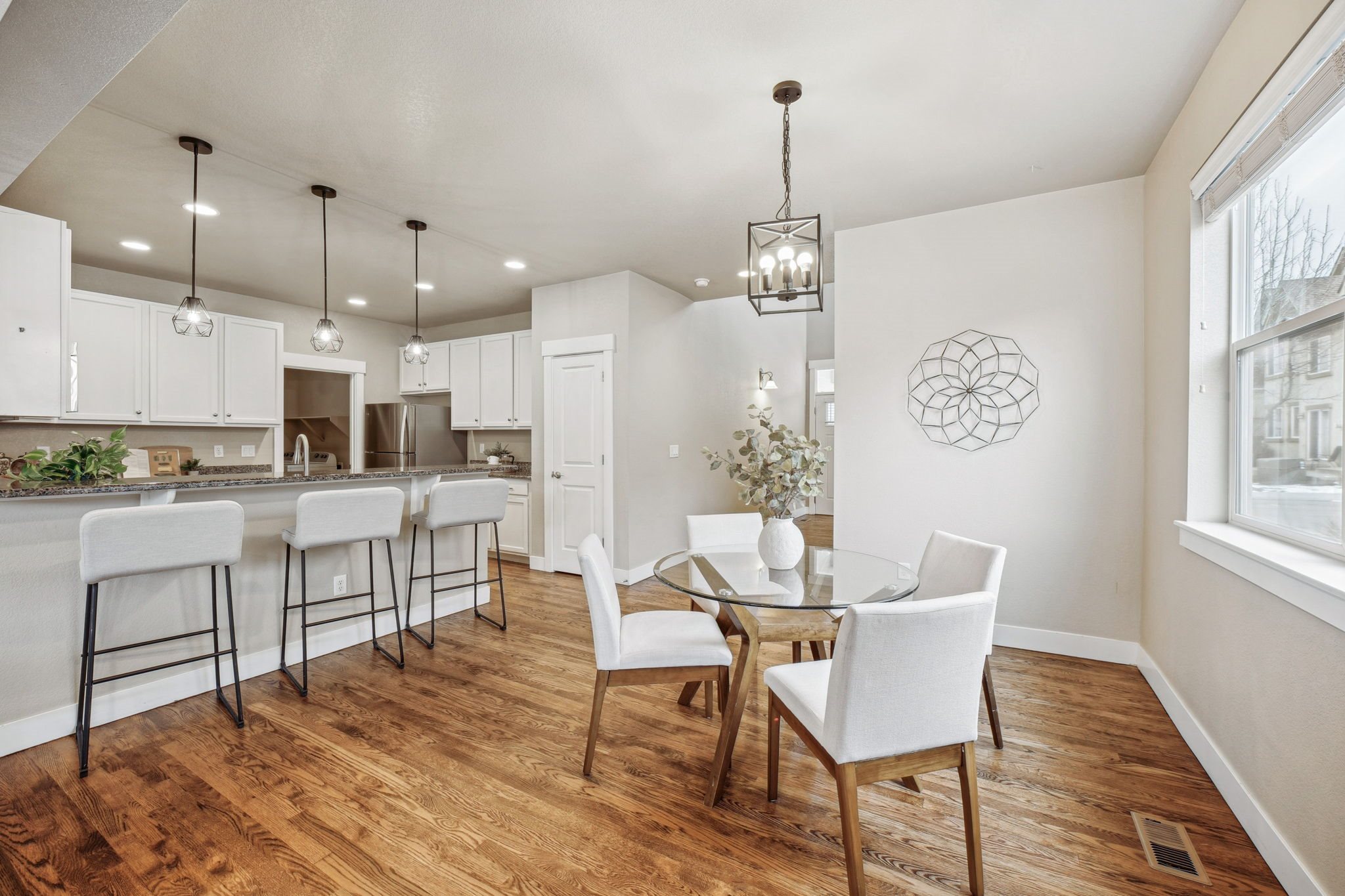 A modern kitchen with white chairs and wooden floors.