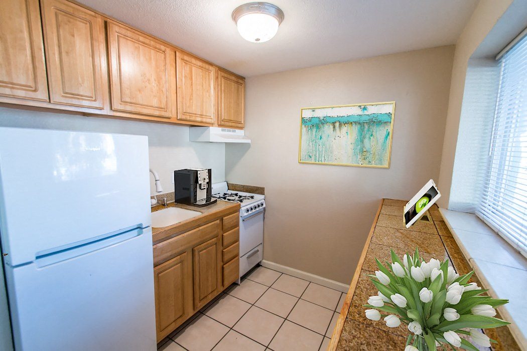 A kitchen with a white refrigerator, wooden cabinets, and a painting on the wall.