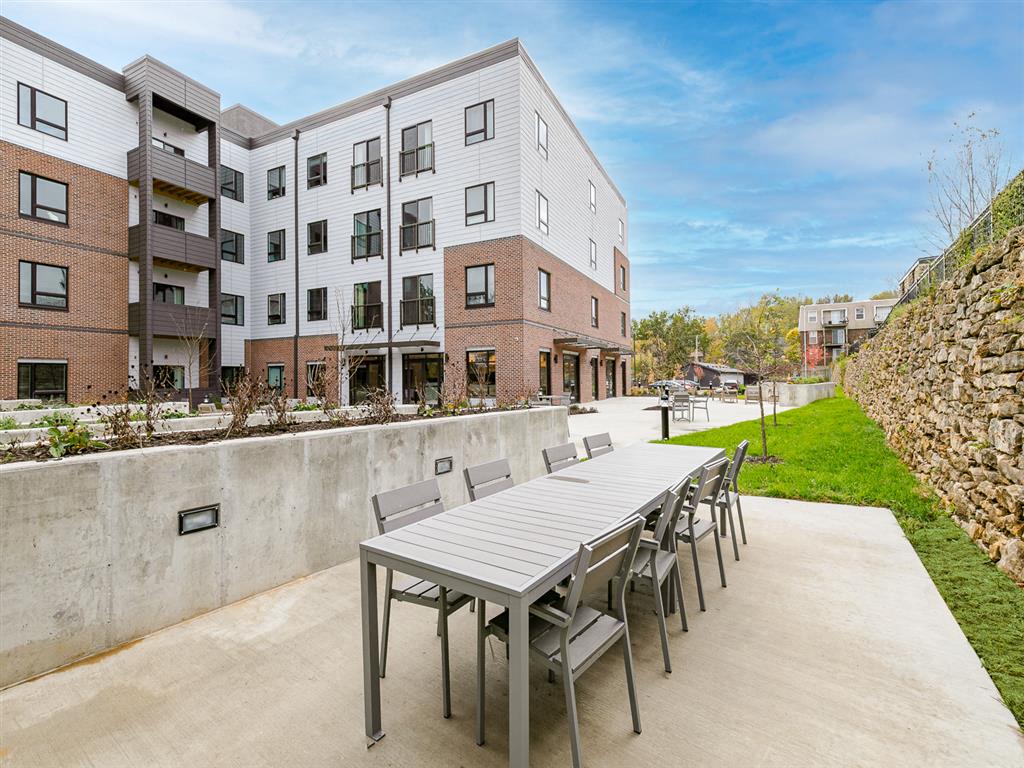 a patio with a wooden table and chairs and a brick building in the background