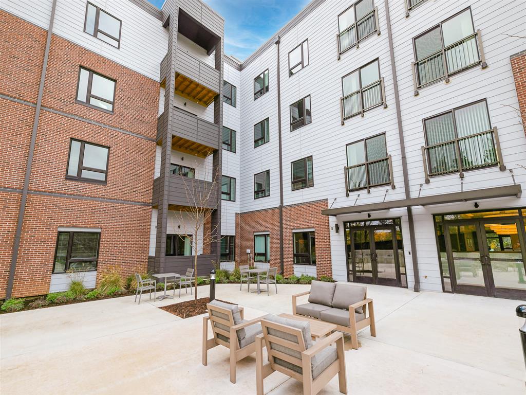 a patio with chairs and a firepit in front of an apartment building