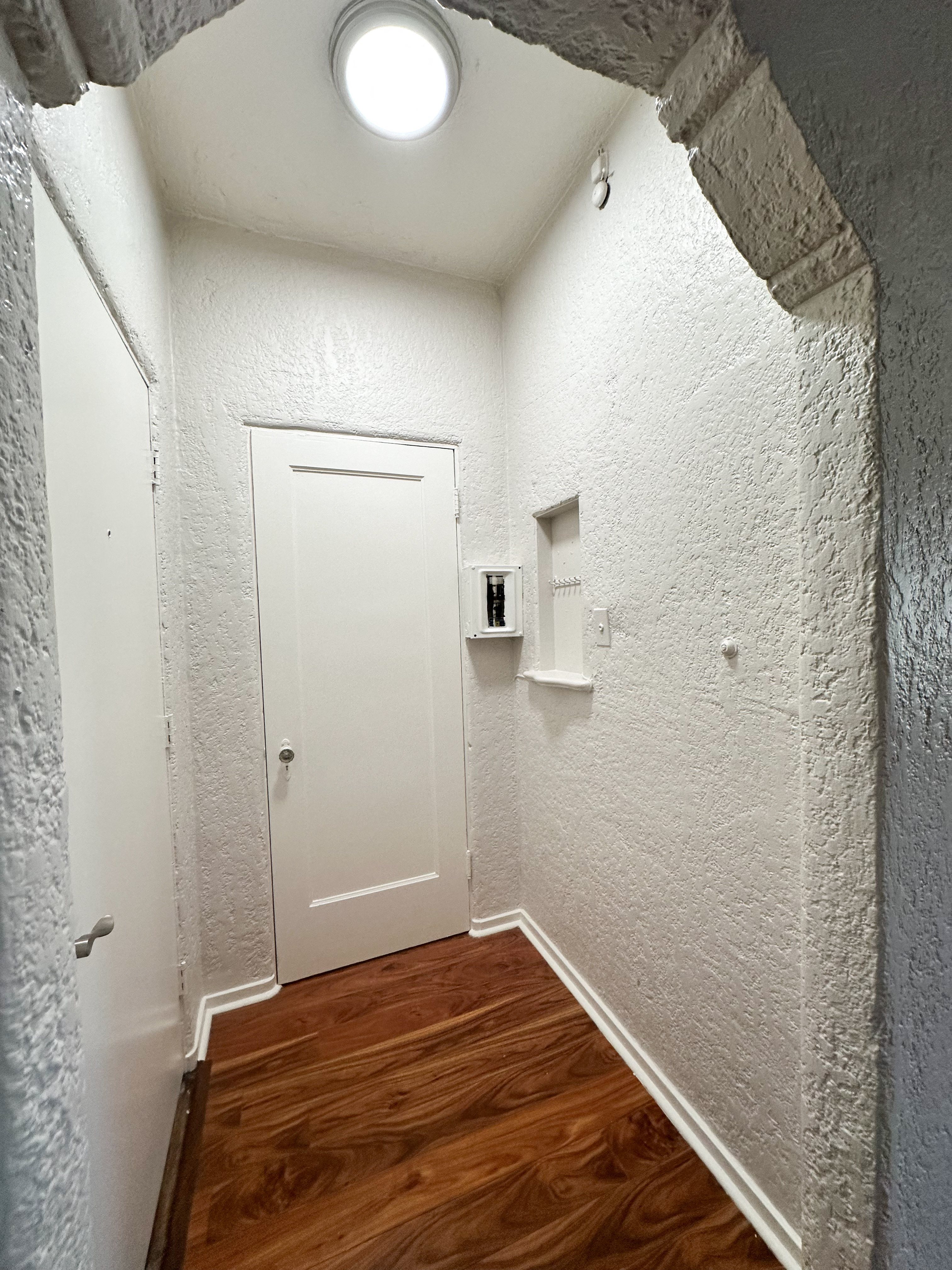 A white door is in a hallway with wood floors and white walls.