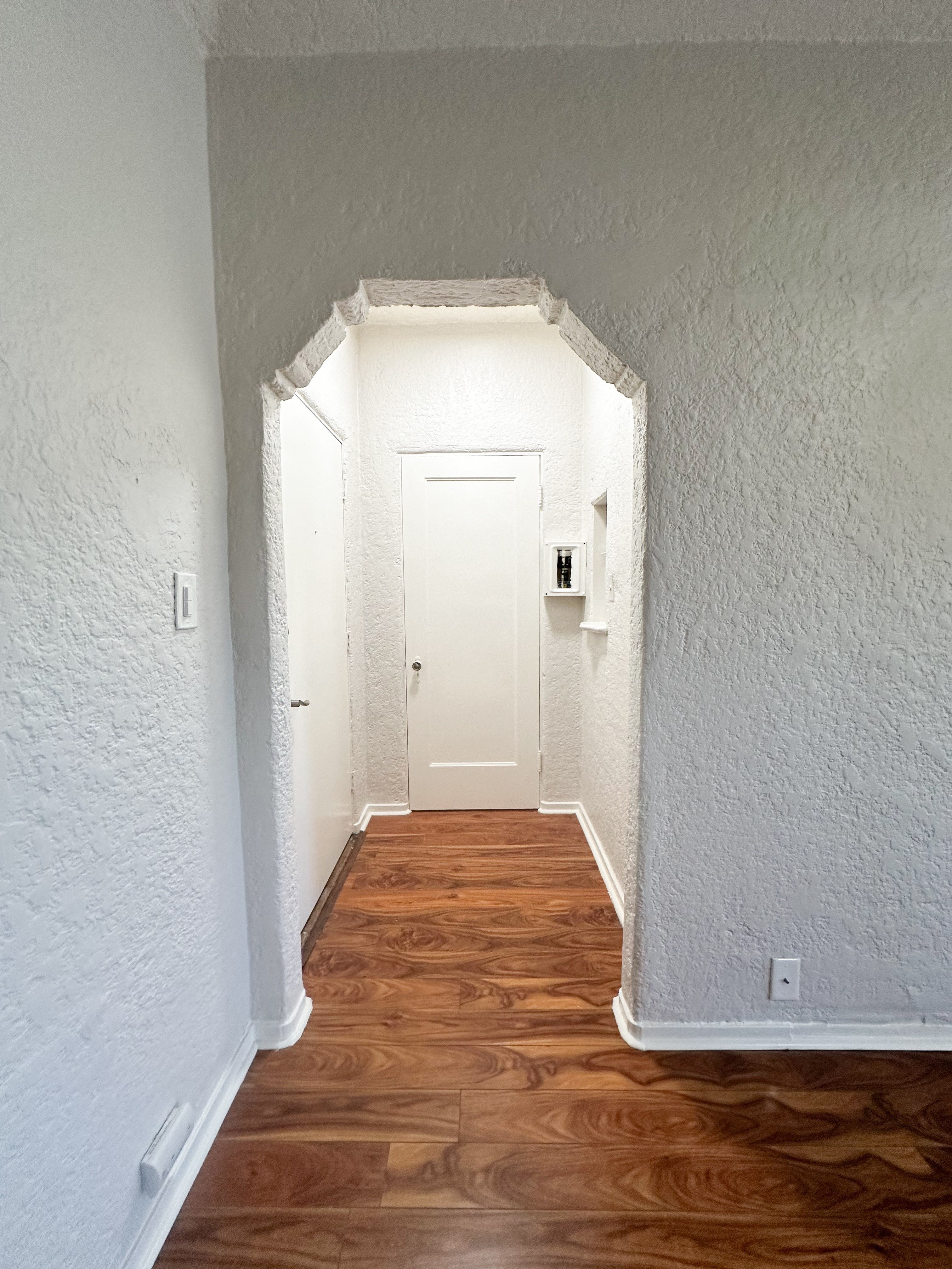 A hallway with a white door and wooden floors.
