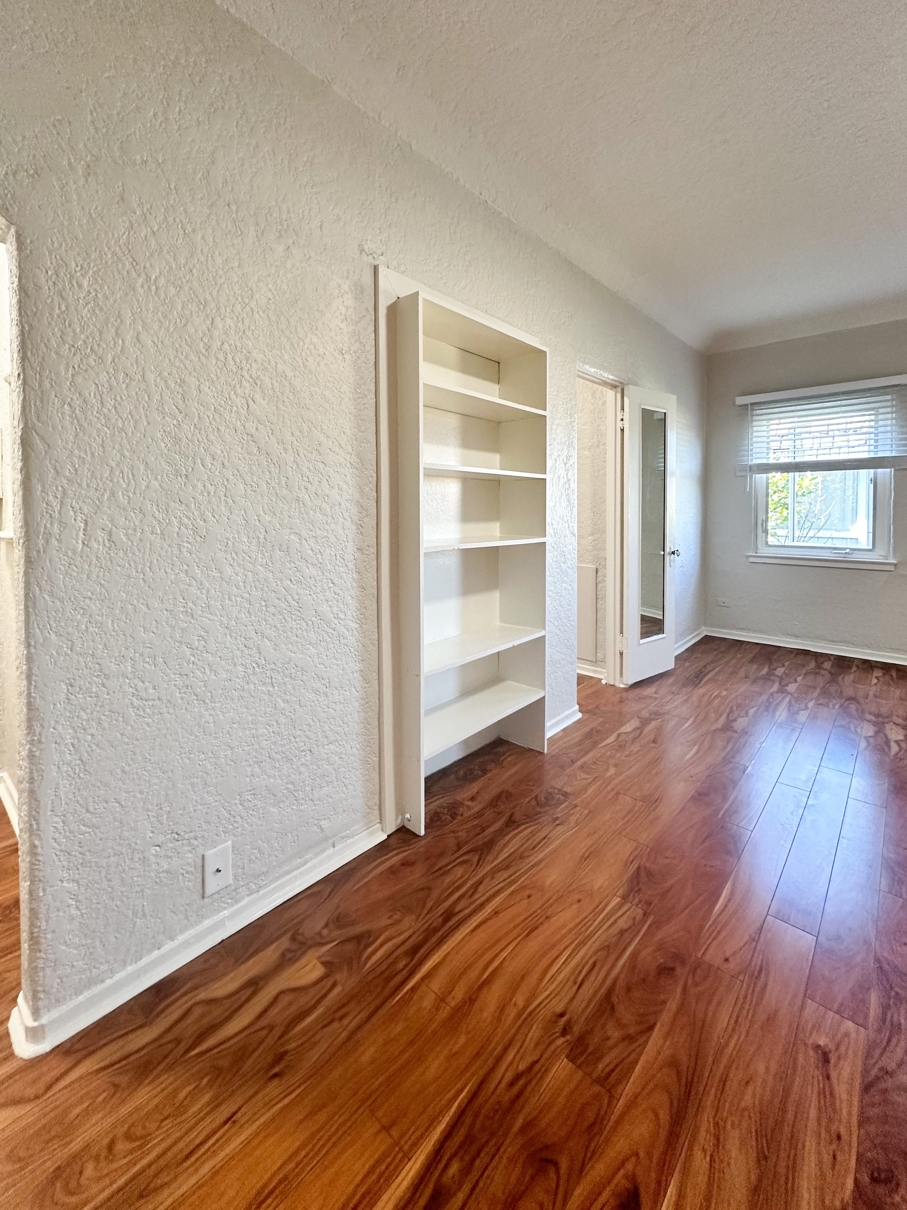 A room with white walls and wooden floors with a window.