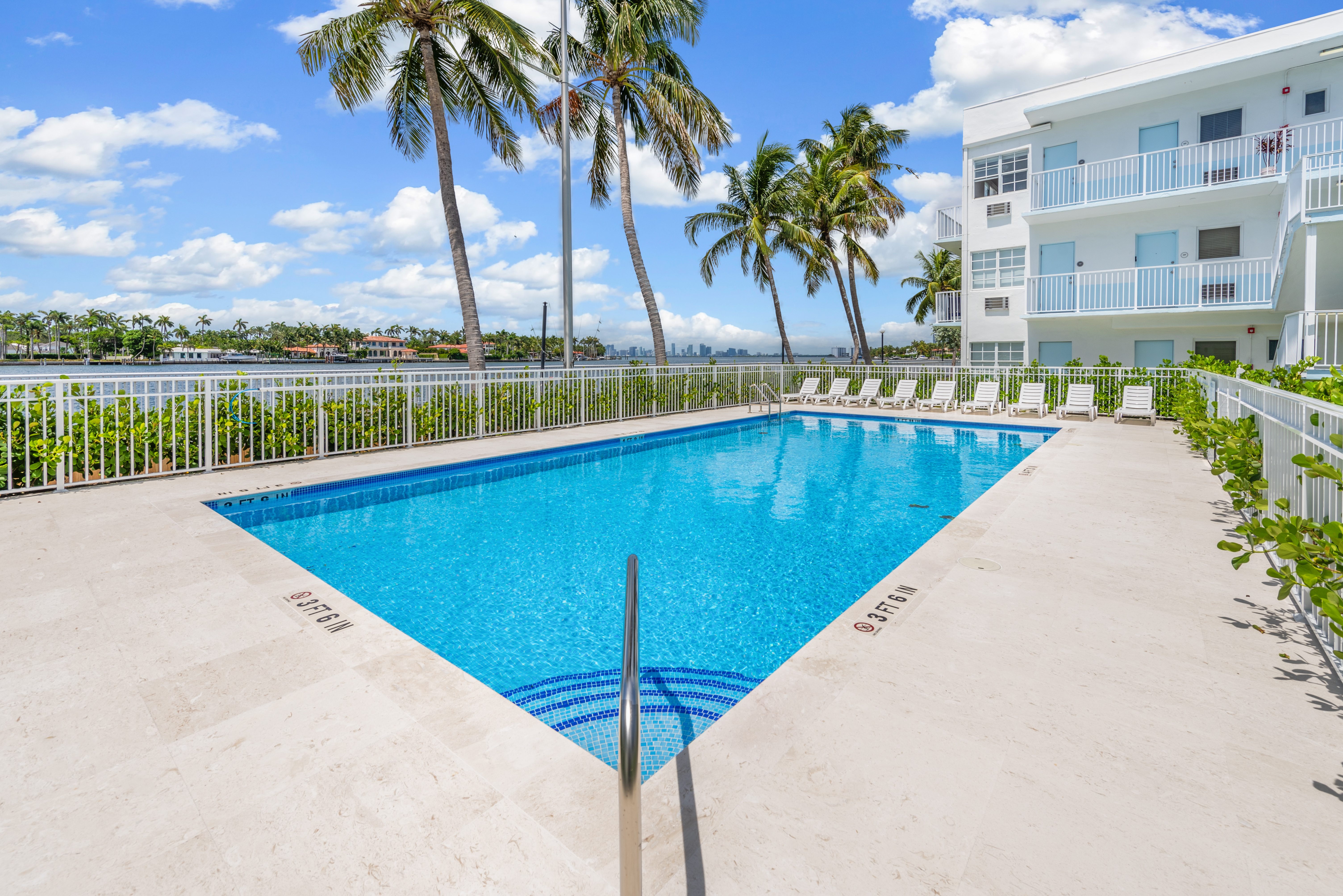 A swimming pool surrounded by palm trees and a white building.