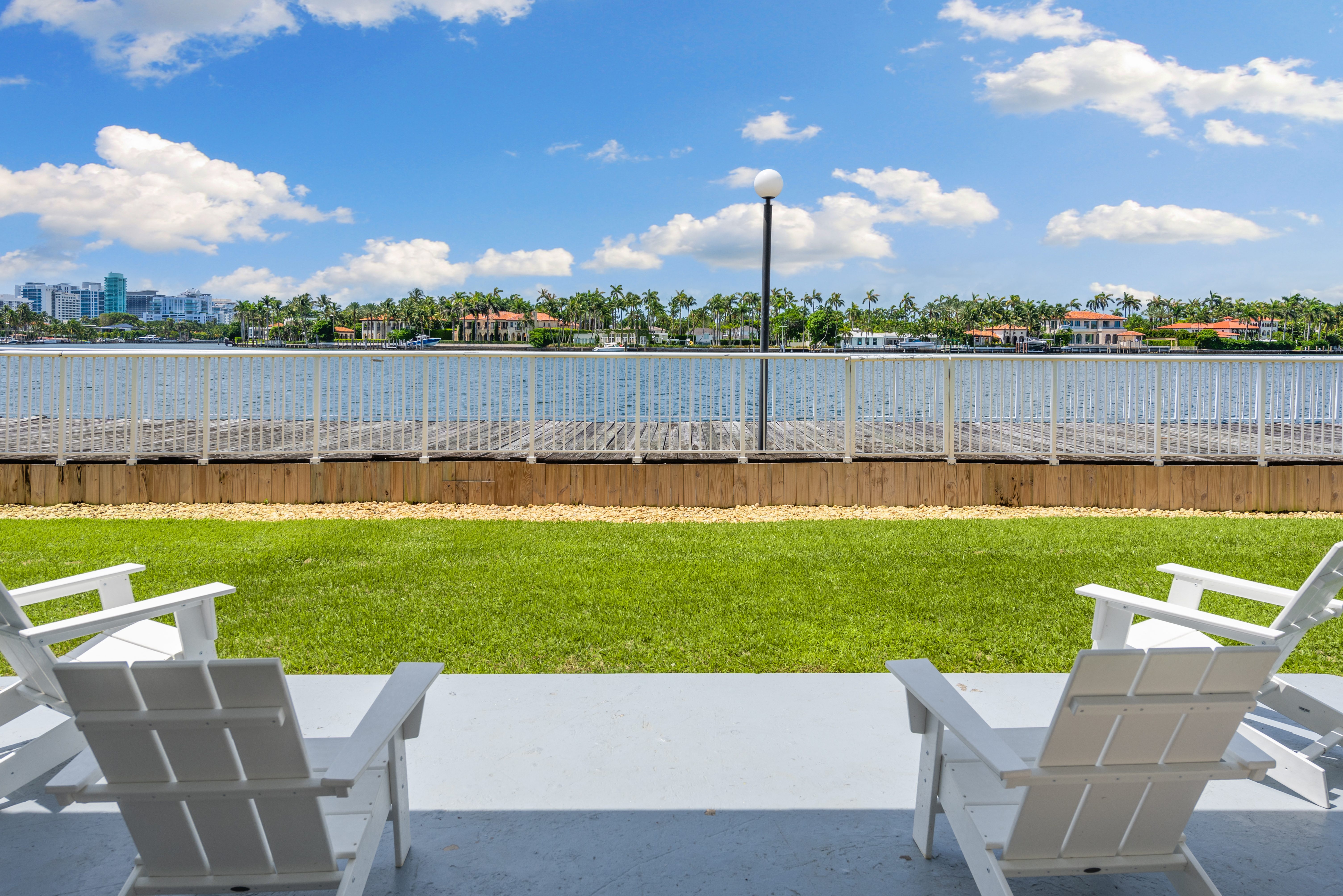 Two white chairs are on a patio overlooking a body of water.