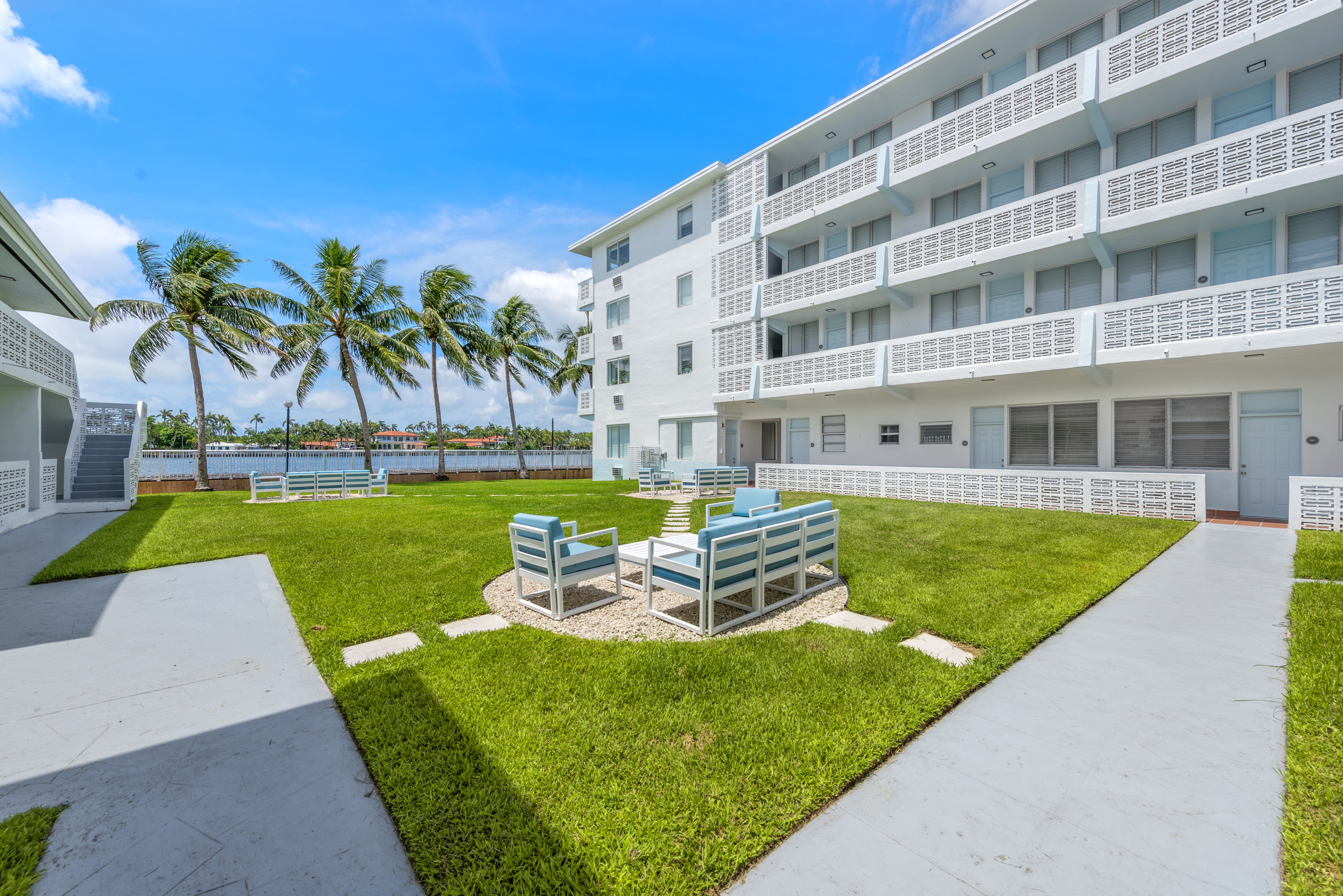A white building with a balcony overlooking a green lawn with a white bench.
