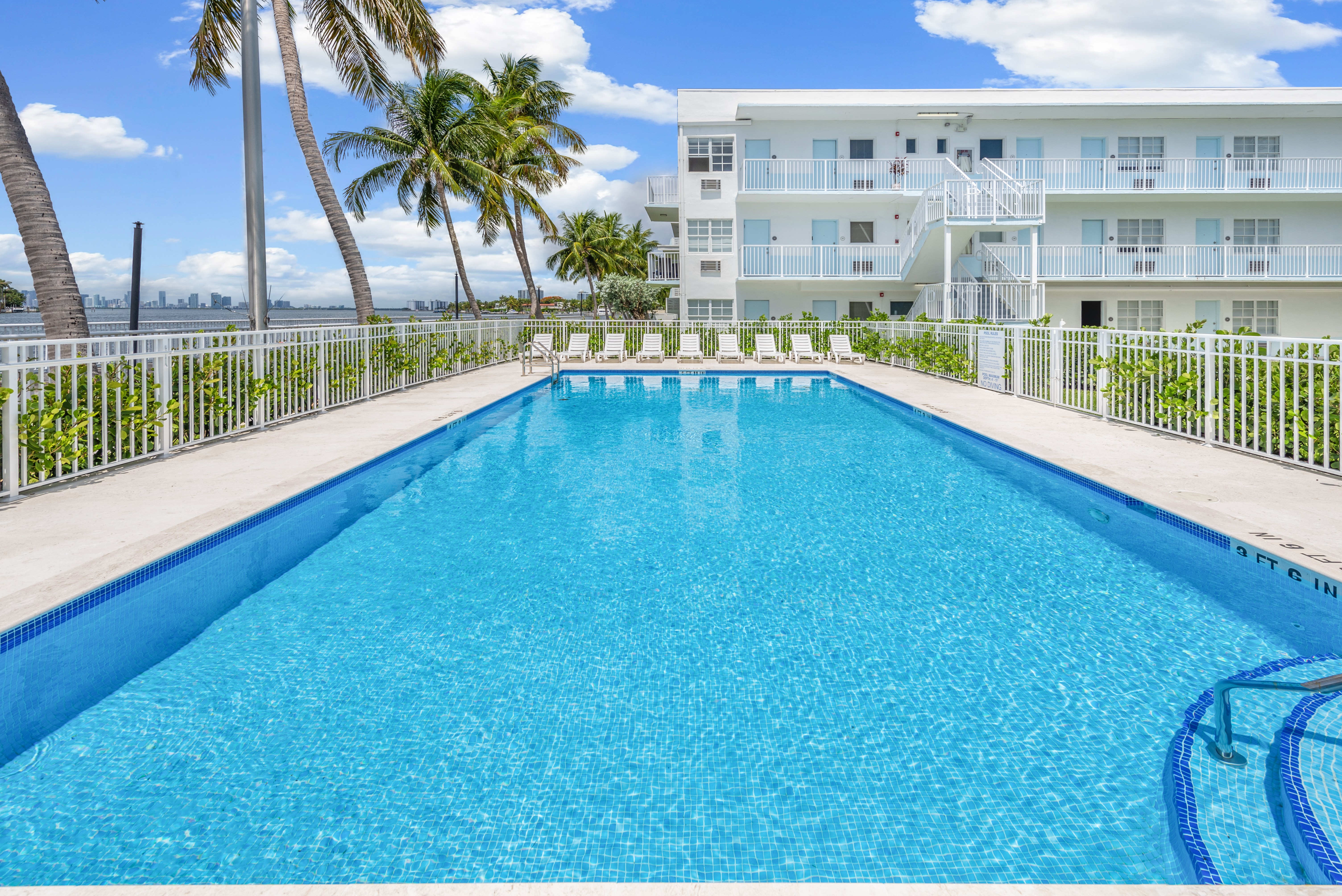 A swimming pool with a white fence and palm trees in the background.